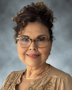 headshot of Isabella Perez, Director of Client Services at Radsource. Isabella's curly hair is piled high atop her head with tendrils framing her face. She wears a tan blouse and turtle-shell-framed eyeglasses and smiles at the camera