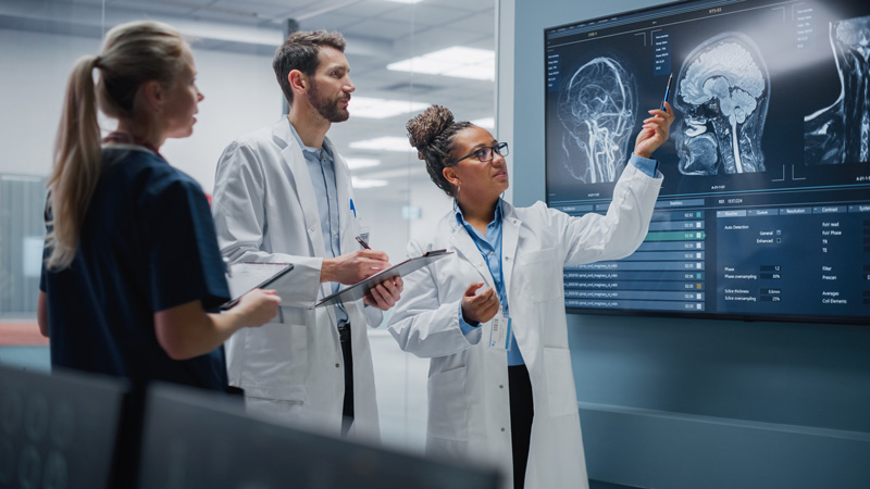 Diverse Team of medical professionals, including a radiologist, Consult a TV Screen Showing MRI Scan images